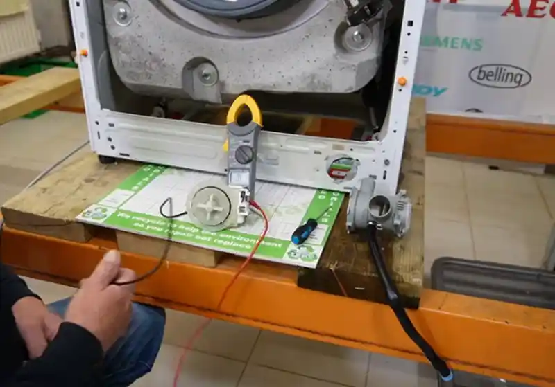 Technician testing washer drain pump motor with a clamp meter